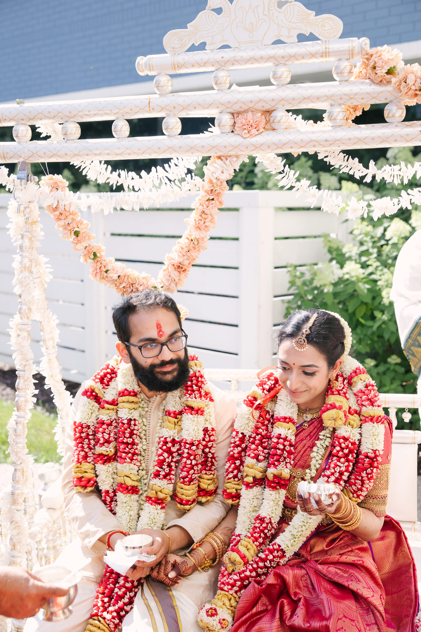 Bride and groom sitting on a ceremonial swing, a munjal, outside of a telugu-tamil hindu ceremony, at a Michigan Indian Wedding. 